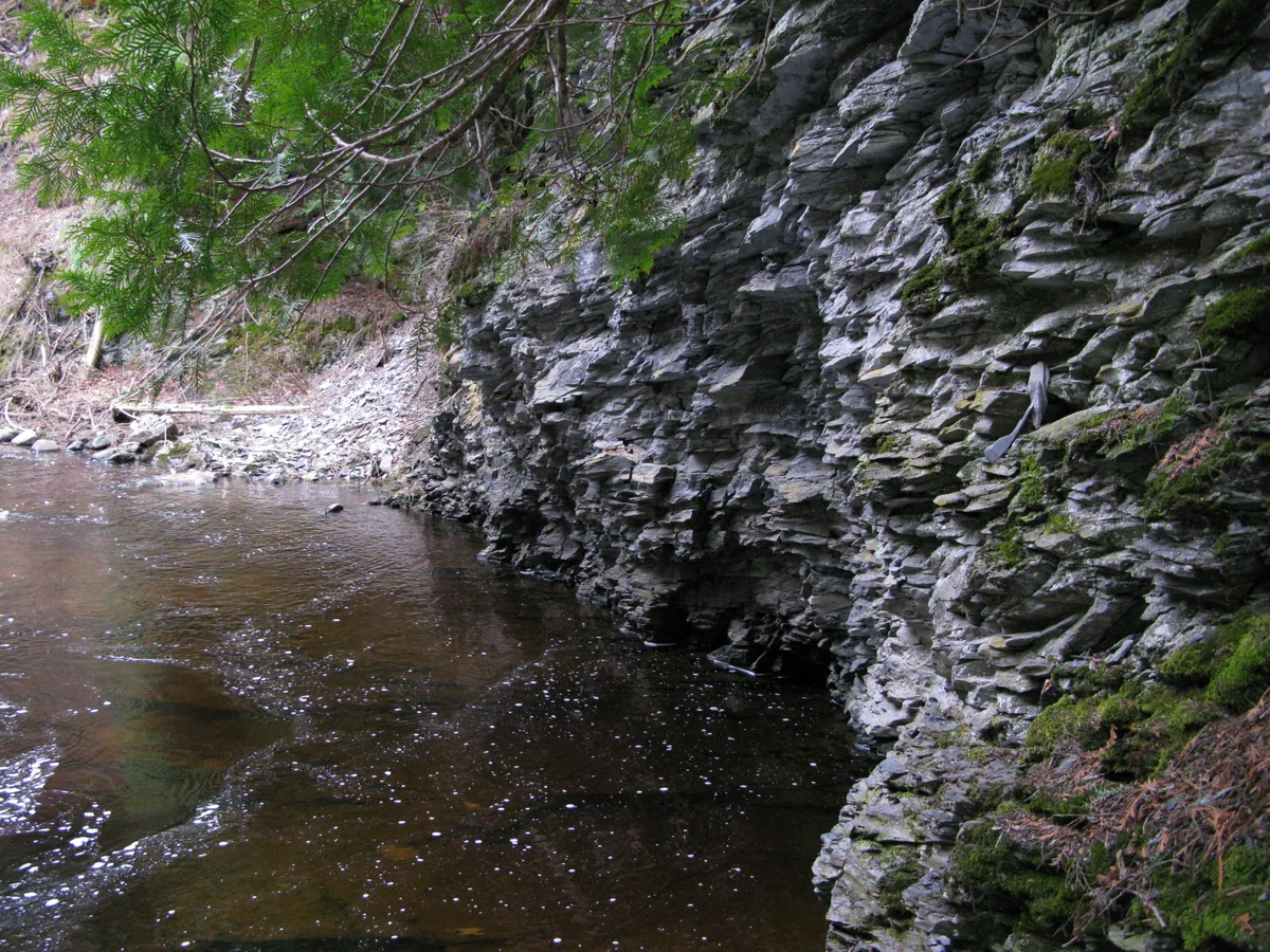Dark pool below a curved wall of jagged slate